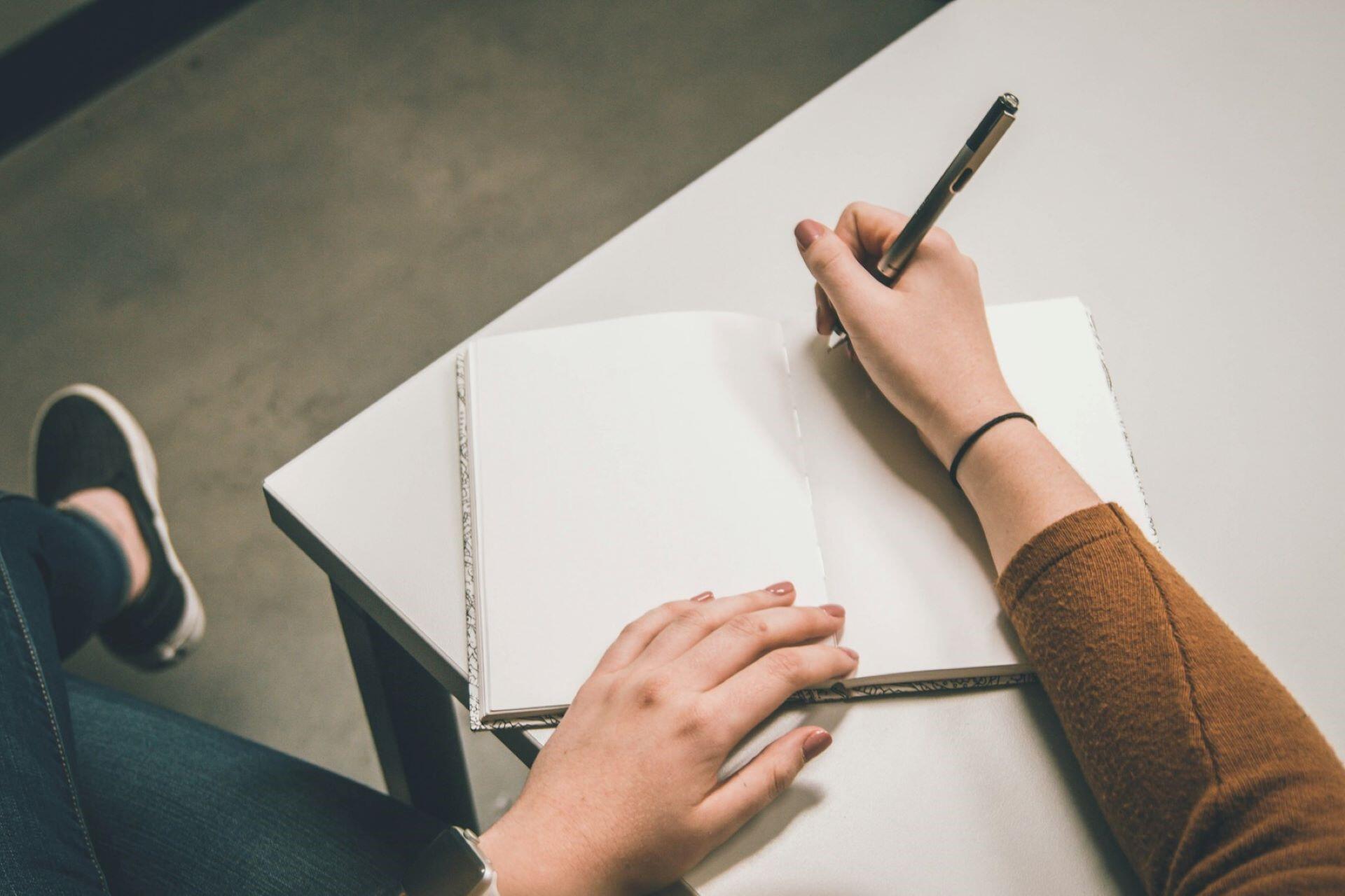 person writing in notebook on desk with pen